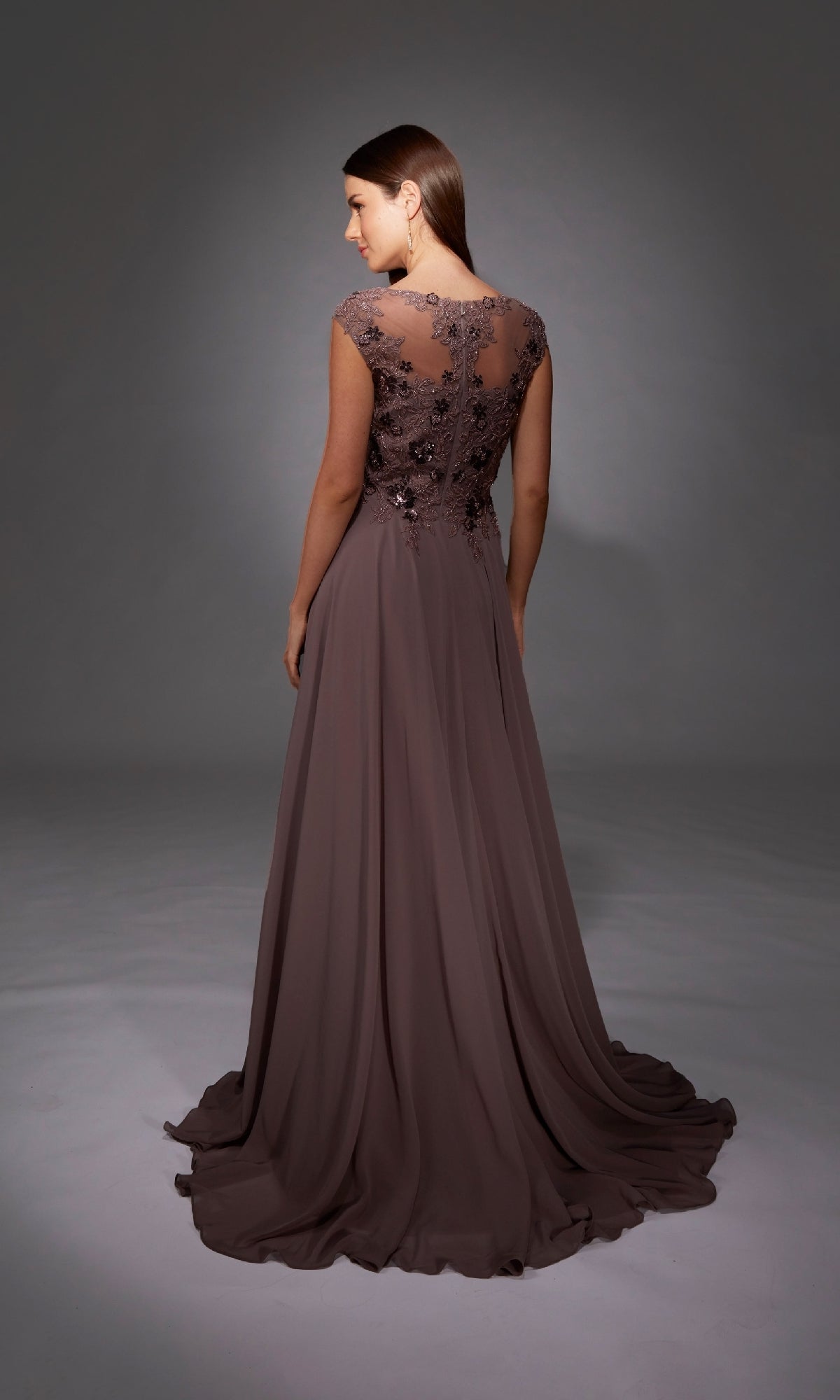 A woman stands facing away in a studio, wearing the Alyce 27842 long mauve chiffon A-line formal dress featuring sheer lace detailing on the back.
